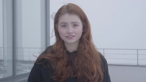 Portrait of a Young Cute Girl with Red Hair in a Dark Coat Standing on the Roof or Terrace of a