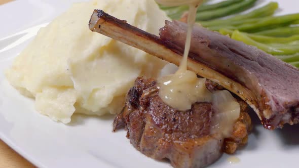 Slider Shot of Adding Sauce to Lamb Cutlets on a White Plate with Mashed Potato and Green Beans