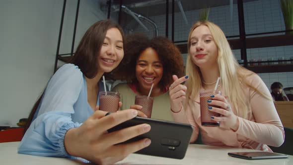 Carefree Diverse Girlfriends Checking Photos on Phone at Cafe