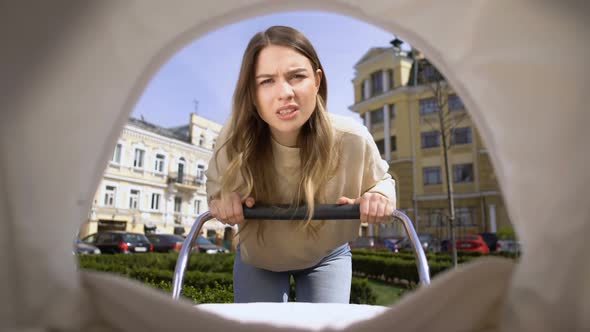 Annoyed Young Woman Trying to Calm Down Crying Infant in Pram, Maternity Stress