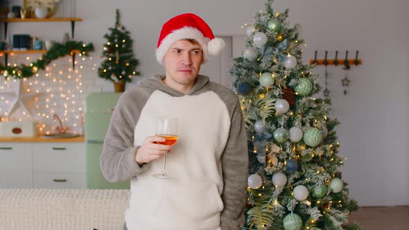 Man in Santa Hat with Glass of Beverage Standing Near Christmas Tree in Living Room