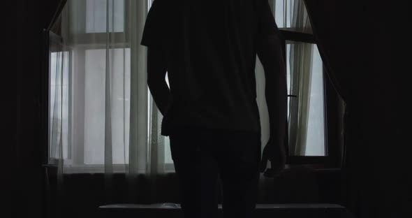 Silhouette of Man Comes to Light Window in Dark Room and Crosses Hands