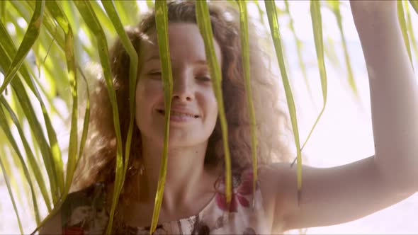 Relaxed Woman Standing Behind Palm Leaves