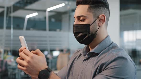 Multiracial Arab Man Guy in Shirt Wear Medical Face Protective Mask in Office Chatting Texting in