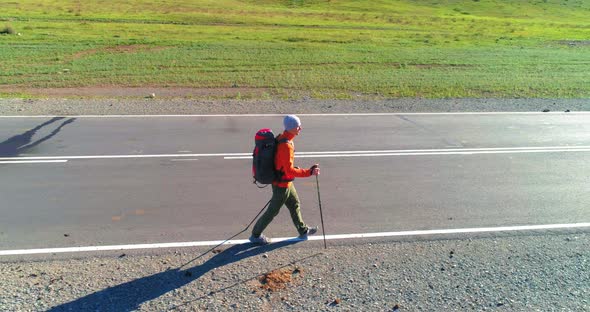 Flight Over Hitchhiker Tourist Walking on Asphalt Road. Huge Rural Valley at Summer Day. Backpack