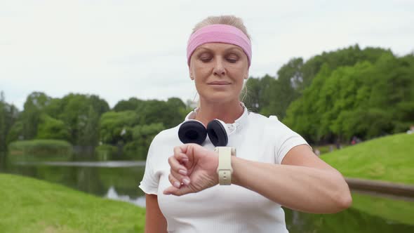 Joyful Mature Woman Using Tracker App on Smartwatch After Workout Outdoors