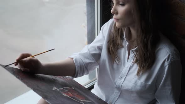 Girl Painter Paints a Picture with Brushes. Portrait of a Cute Girl in a Home Studio