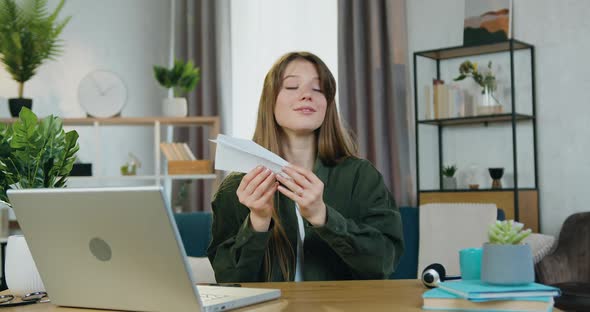 Female Person Sitting at the Table in Cozy Home Office and Launching Paper Airplane Flying