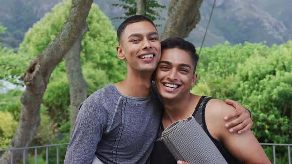 Portrait of happy mixed race gay male couple standing in garden embracing and laughing