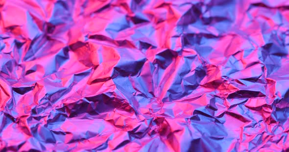 Wrinkled aluminum foil under red and purple lighting in rotation