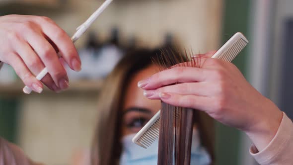 Female hairdresser wearing face mask cutting hair of female customer at hair salon