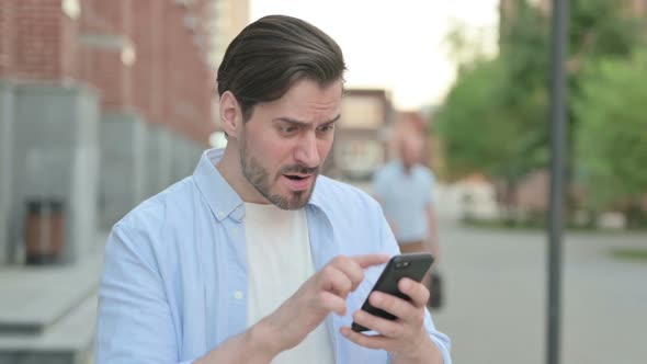 Man Reacting to Loss on Smartphone While Standing Outdoor