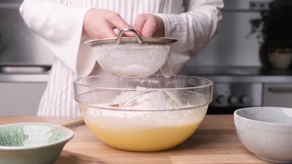 Woman Sifting Flour Through Sieve Into A Glass Bowl With Mixture. Preparing Carrot Cake In The Kitch