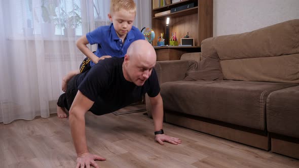 A Strong Father Doing Pushups with His Son on His Back at Home on the Floor