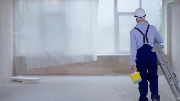 Man with Stepladder and Can of Paint in His Hands Prepares To Paint Walls During an Indoor