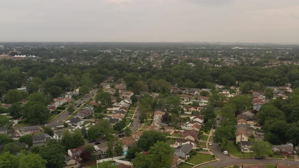 An aerial view over a suburban neighborhood on a cloudy day. The camera dolly in and tilt down over