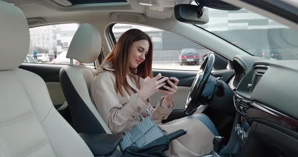 Excited Young Woman Hold Phone Chatting in Dating App Feel Happy Sit in Car Euphoric Overjoyed Lady