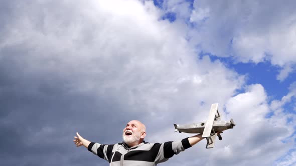 Happy Senior Man Pretend Flying on Wooden Airplane in Sky Freedom