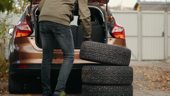 A Man Puts Winter Tires in the Trunk of a Car