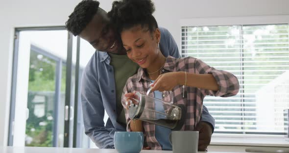 Video of happy african american couple preparing coffee and embracing at home