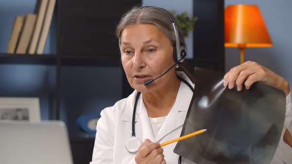 Aged Female Doctor Wearing Headset and Explaining X-ray To Patient Online