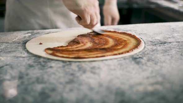 Professional Chef is Cooking Pizza Applying Delicious Tomato Sauce on Dough with a Spoon