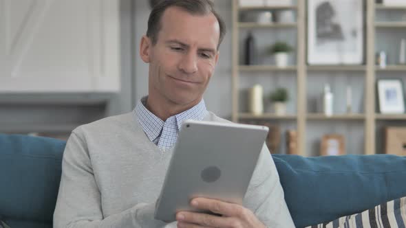 Middle Aged Man Using Tablet while Relaxing on Couch