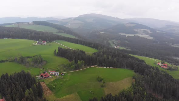 Flying Over a Small Village on the Austrian Green Hills in Foggy Weather