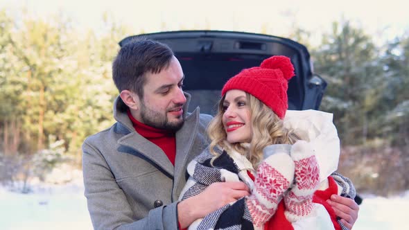 Young Couple a Man and a Woman Hugging Near the Car in a Winter and Drinking Coffee Snowy Forest