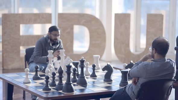 Two Multiethnic Young Men are Playing Chess at Table in Modern Office Irrl