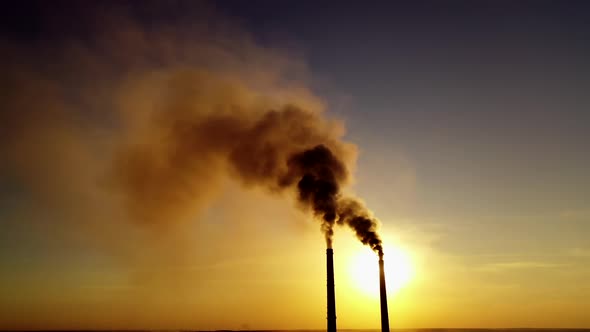 Two industrial pipes with dark smoke at sunset. 