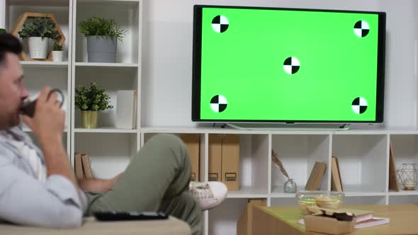 Man Drinking Tea and Watching TV with Green Screen at Home