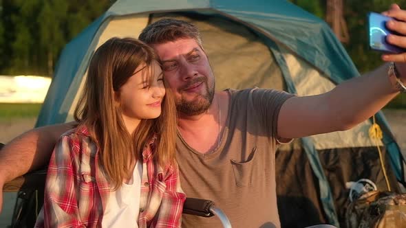 father and daughter take selfie against background of tent on a hike