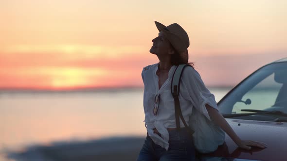 Relaxed Backpacker Smiling Woman Enjoying Natural Seascape at Sunset During Car Travel Medium Shot