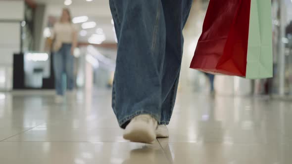 Woman Legs in Loose Jeans with Shopping Bags Walking in Mall