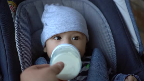 A Baby in a Stroller Sucks Milk From a Bottle