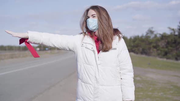 Portrait of Pretty Brunette Caucasian Woman in Protective Face Mask Hitchhiking on Empty Suburban