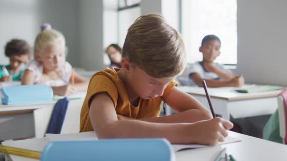 Video of focused caucasian boy sitting at desk in classsroom