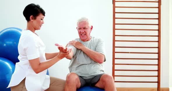 Smiling Physiotherapist Helping Elderly Patient Stretch Arm