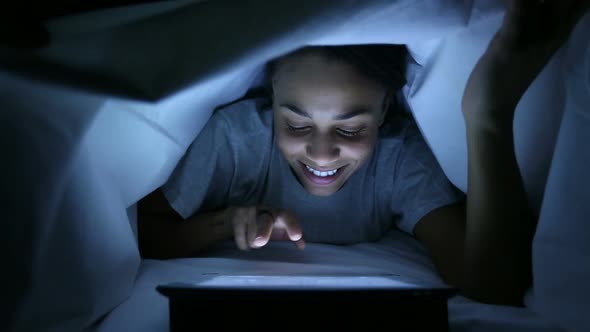 Furtive Woman Using Digital Tablet under Bed Sheets