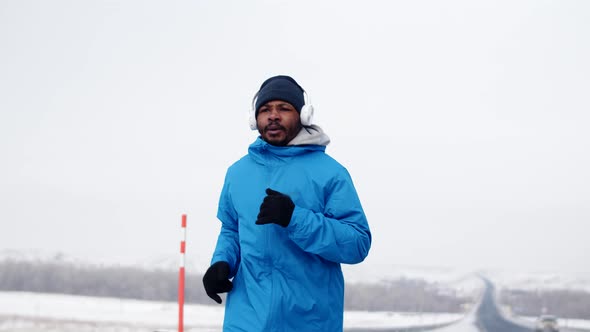 Black Man in Warm Clothes Runs Sport Along Road Doing Cardio Training and Runs Away From Frame Front