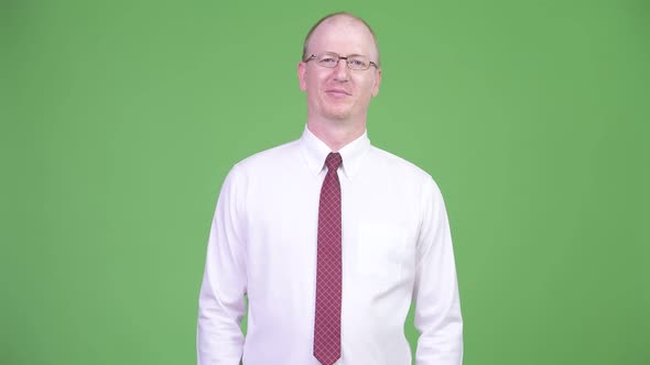 Happy Mature Bald Businessman Wearing Eyeglasses Against Green Background