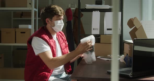 Man Wearing Red Vest Protective Mask Employee of Warehouse Packing Parcel Into Delivery Box and