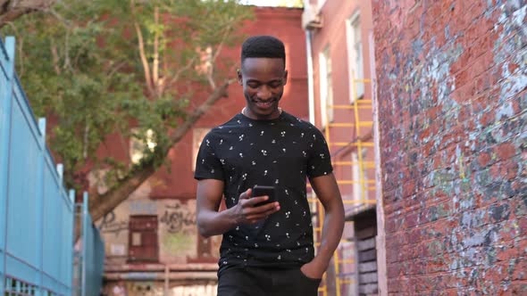 A young black guy is walking around his neighborhood. A man walks down a city street