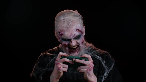 Sinister Man Halloween Zombie Enthusiastically Playing Racing Drive Video Games on Mobile Phone