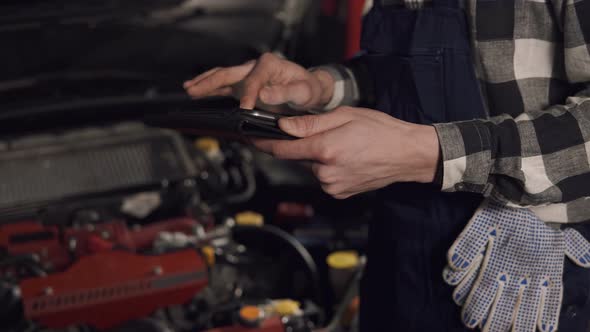 Close Up Footage in Slow Motion of Auto Service Technician Using Digital Tablet to Examine the