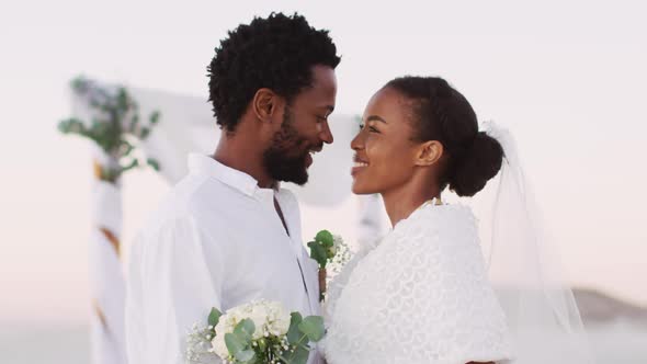 African american couple in love getting married, smiling and looking at other on the beach
