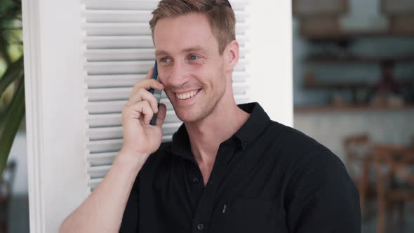 Portrait of Businessman in Black Shirt in Stylish Cafe and Talking on Phone