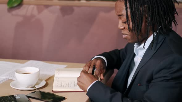 Focused Businessman Worjing at a Cafe with Laptop and Papers