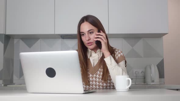 Young Busy Businesswoman at Her Desk Talking on the Phone and Looking at Computer of the Modern
